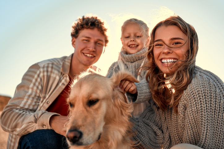 A young couple of parents with a little cute daughter and their beloved retriever dog walking and relaxing on a sandy beach in cool weather on their weekend. Family traveling with pet.
