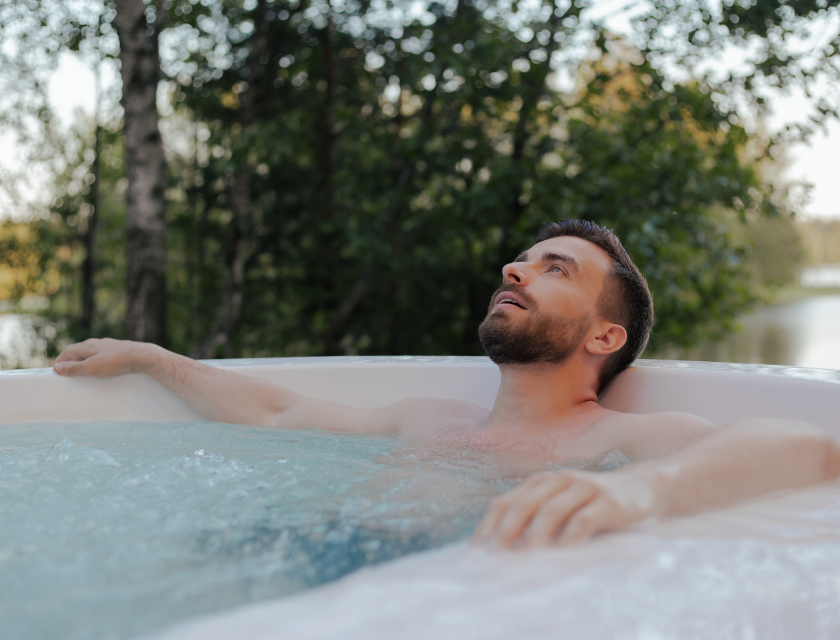Man relaxing in an outdoor hot tub, surrounded by tranquil trees and nature.