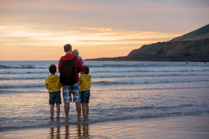 Young father with his beautiful children, enjoying the sunset over the ocean on a low tide in Devon, England