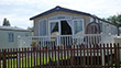 Static caravan with a veranda in a British holiday park, featuring large windows and a fenced garden area with outdoor seating.