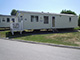 Static caravan in a British holiday park, situated on a grassy plot next to a paved road, with other caravans visible in the background.